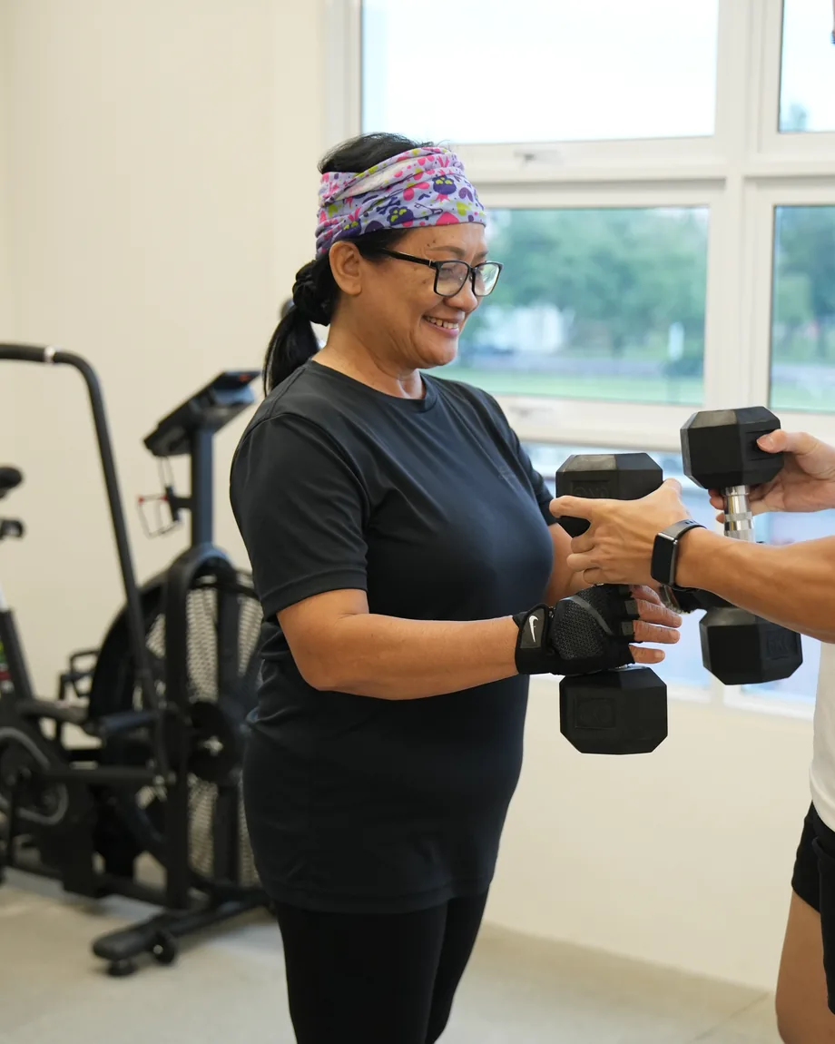 iLift coach handing dumbbells to a smiling older adult client, Kuching.