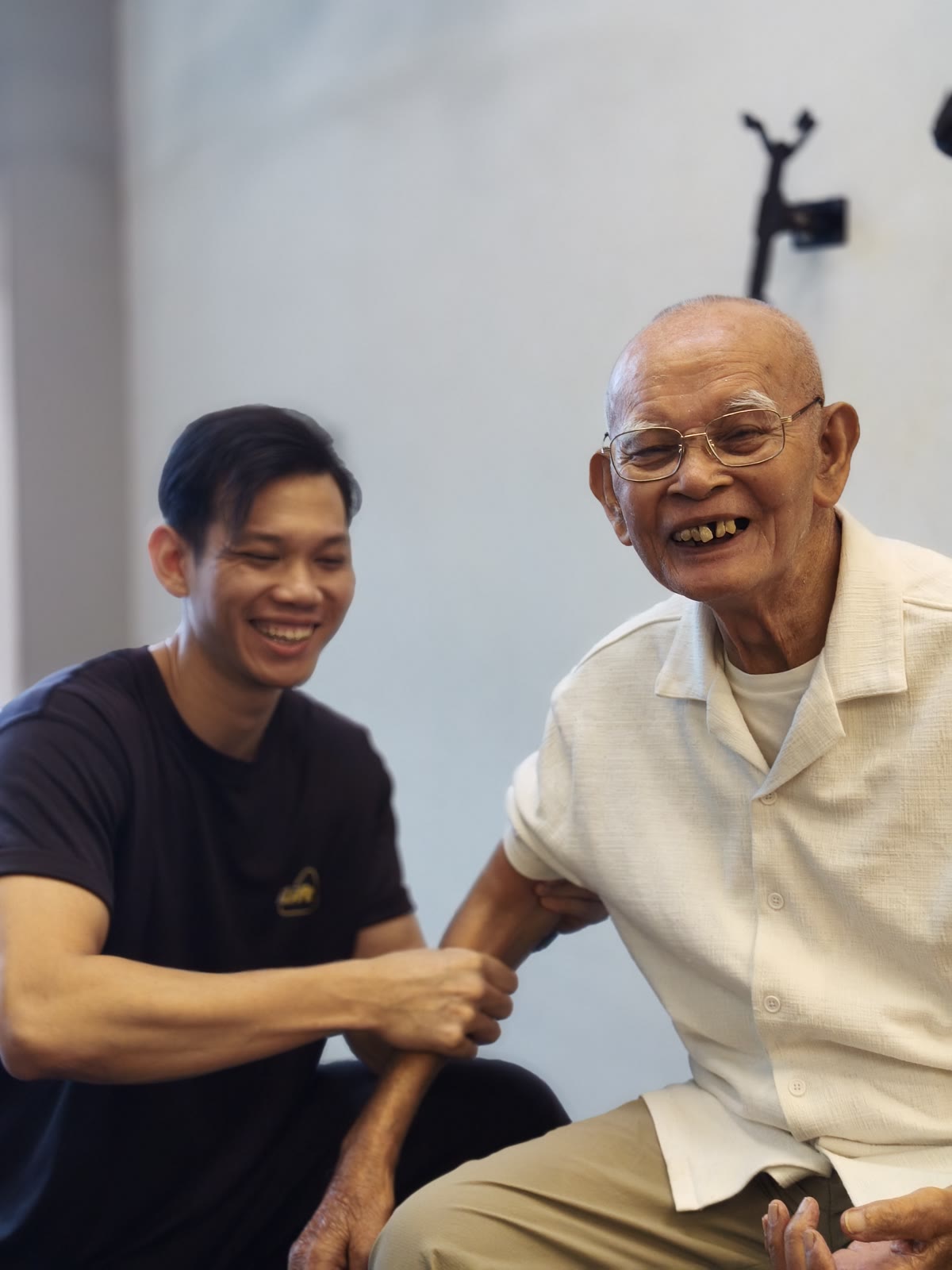 Wan, in his 80s, laughing and fist-bumping Coach Matiin at iLift Gala City